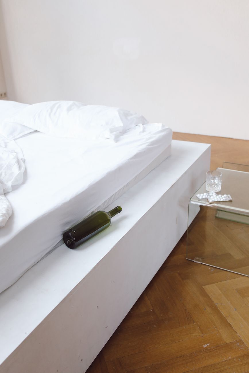 photo of an empty bottle beside a white bed