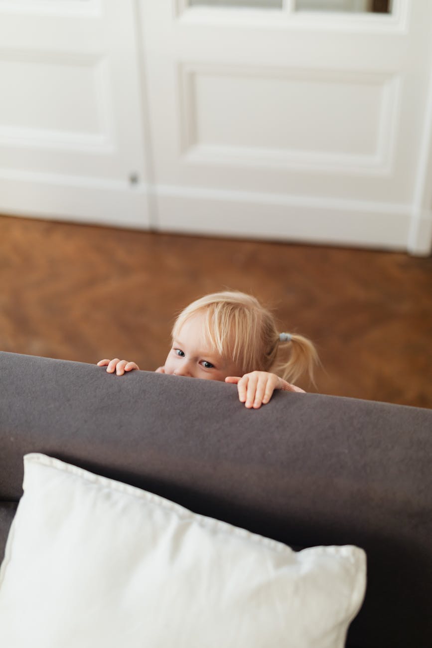 girl hiding behind the gray sofa