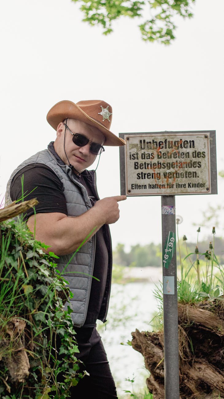 man in cowboy hat with sheriff star pointing at information sign